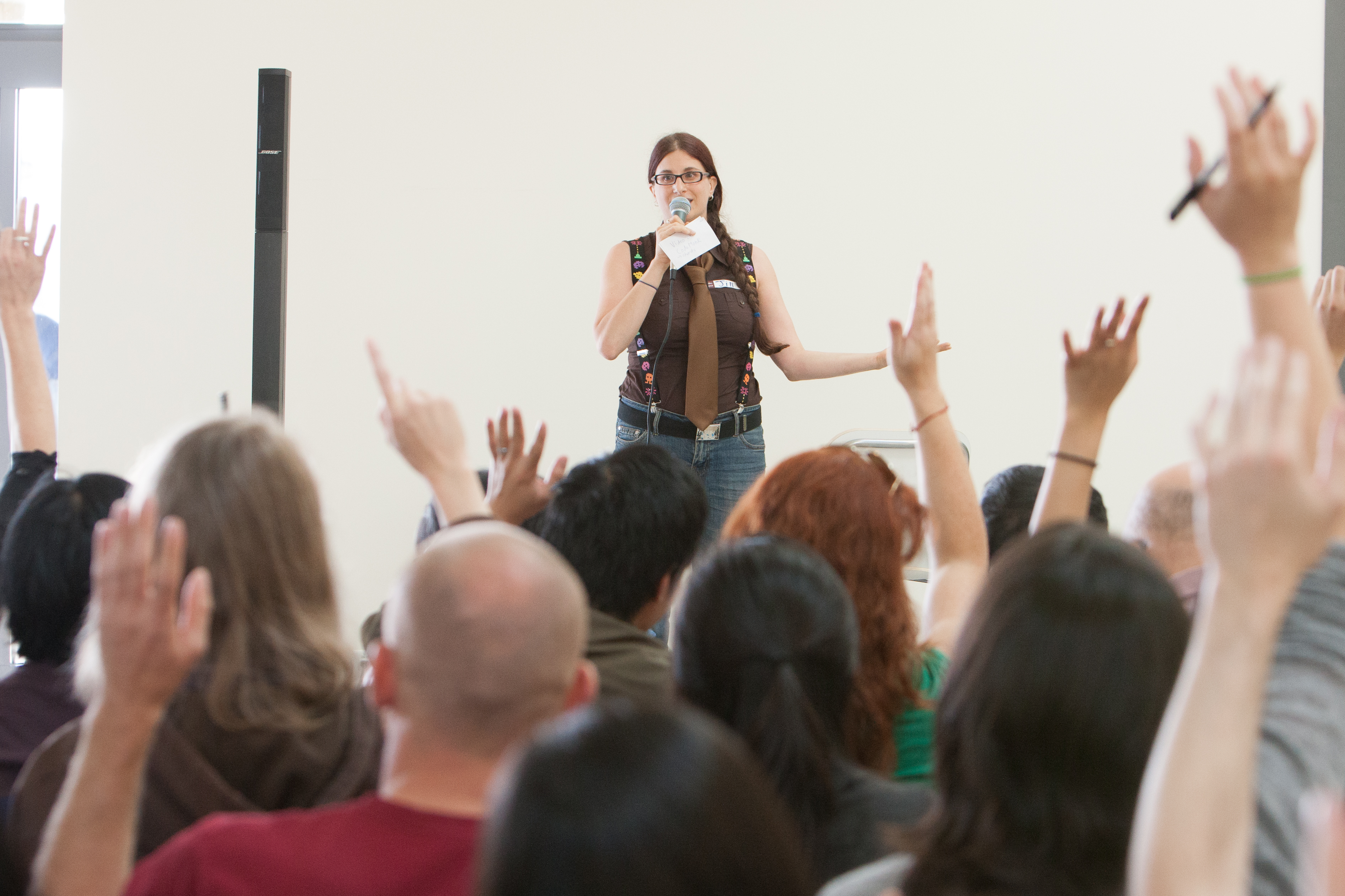 A woman holding a microphone, in front of a lot of people with raised hands.