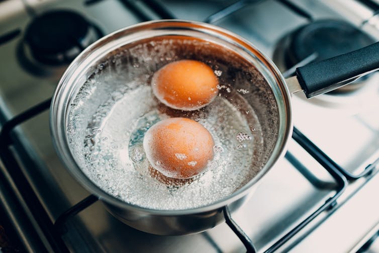 Eggs boiling in a pot on a gas cooktop.