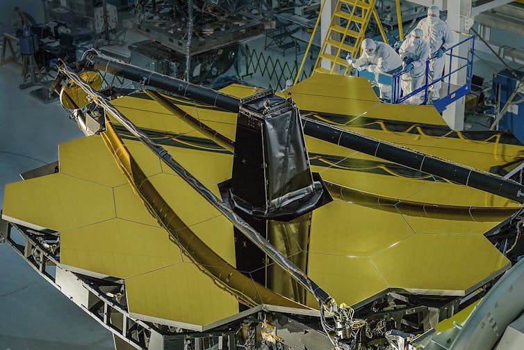 A moody image of the honeycomb-like mirror layout still in a lab with people in protective gear inspecting it.