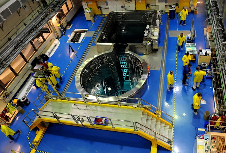 People wearing yellow coats in a large scientific laboratory.