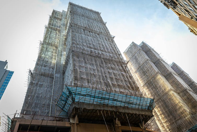 A high-rise apartment covered in bamboo scaffolding and white mesh.