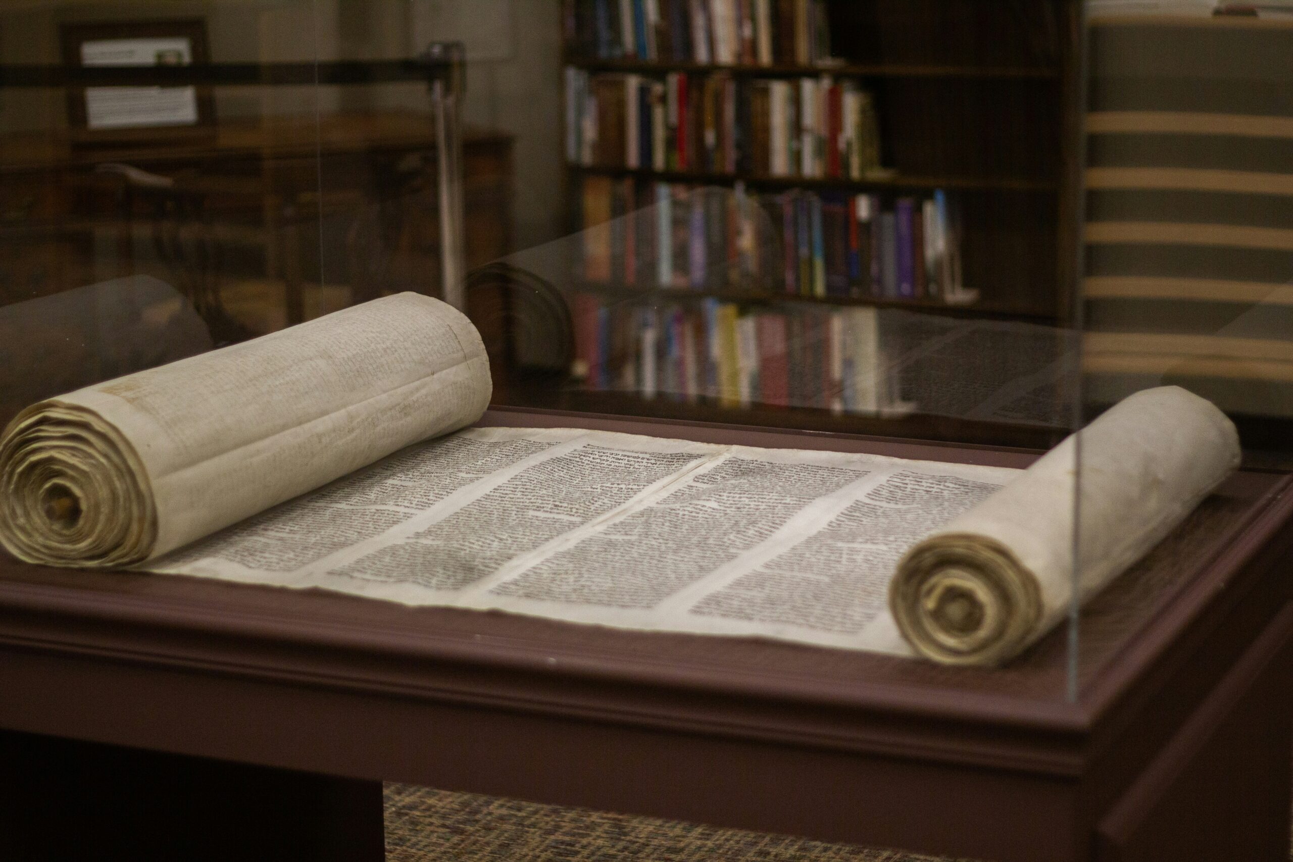 Photo of an ancient scroll partially unrolled inside a glass case on a wooden desk.