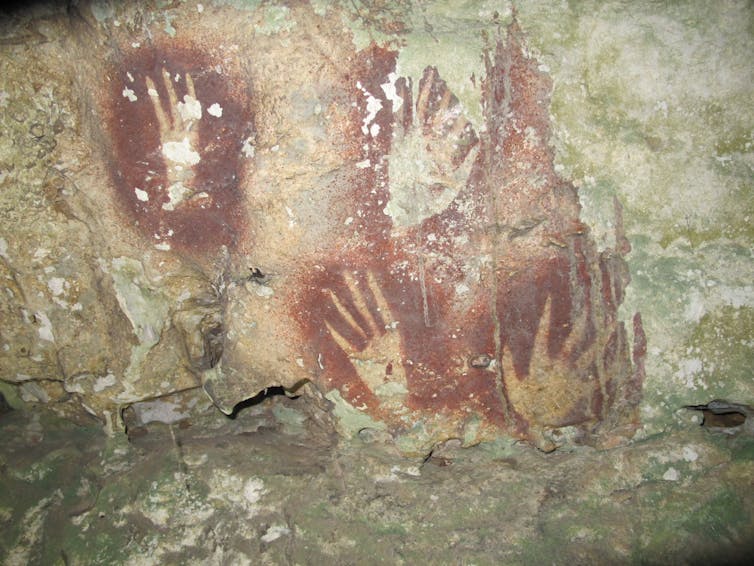 A rocky surface with hand stencils surrounded by red pigment, fingers narrow.